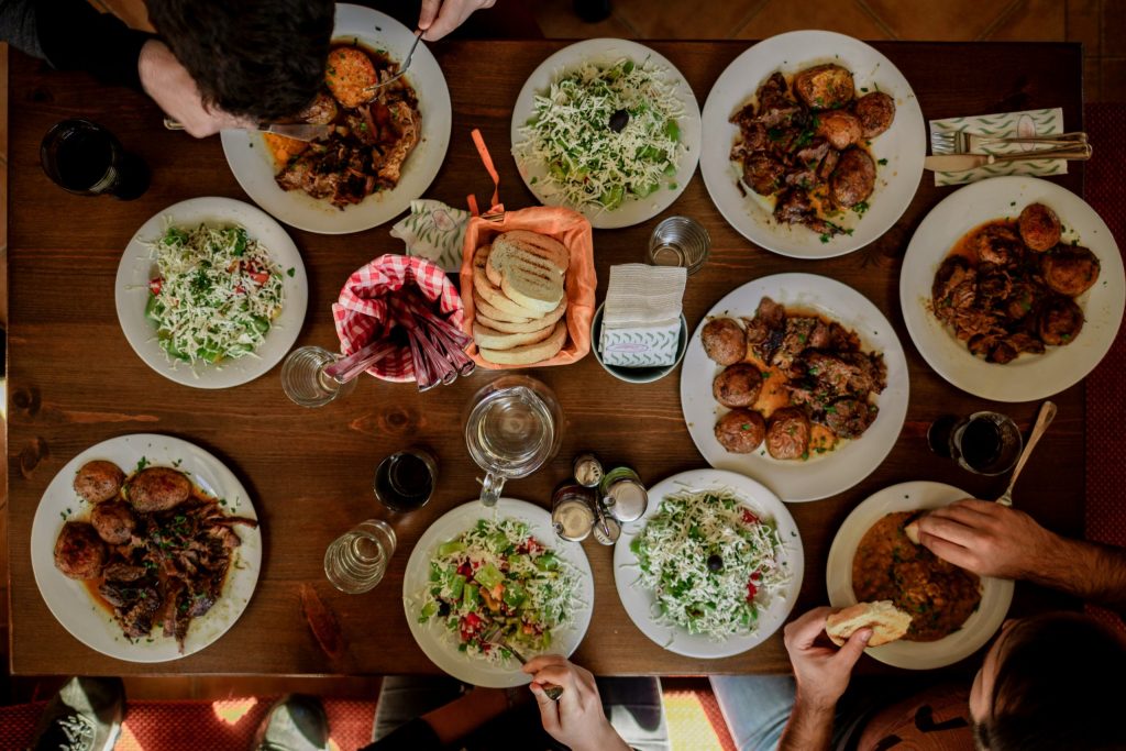 Overhead view of friends sharing a restaurant-style meal at home, with plated dishes, salads and bread on a beautifully set dining table