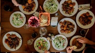 Overhead view of friends sharing a restaurant-style meal at home, with plated dishes, salads and bread on a beautifully set dining table