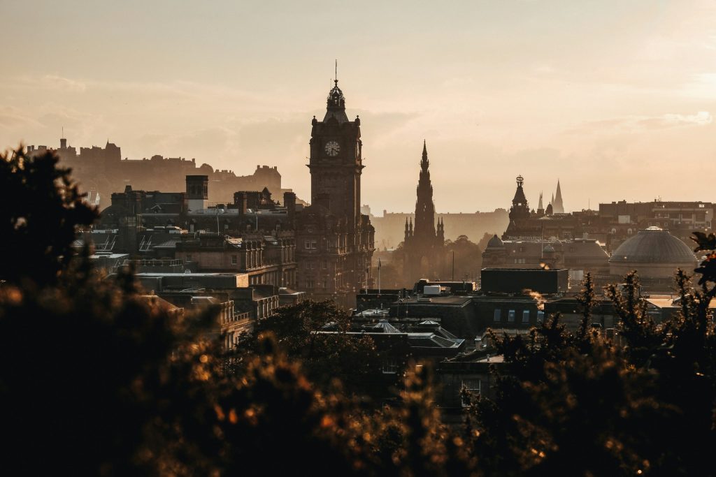 Golden-hour view over Edinburgh skyline with the Balmoral clock tower, Scott Monument and Edinburgh Castle silhouetted in the distance.