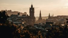 Golden-hour view over Edinburgh skyline with the Balmoral clock tower, Scott Monument and Edinburgh Castle silhouetted in the distance.