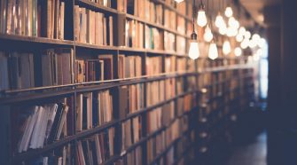 Warmly lit library aisle with rows of bookshelves and hanging bulbs creating a soft, atmospheric glow.