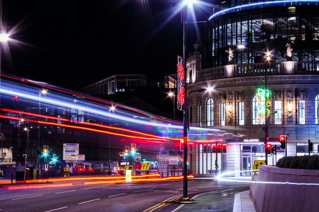 Alt text: Night-time view of Leeds city centre with colourful light trails passing the Majestic building.