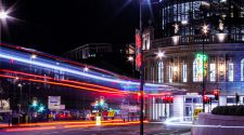 Alt text: Night-time view of Leeds city centre with colourful light trails passing the Majestic building.