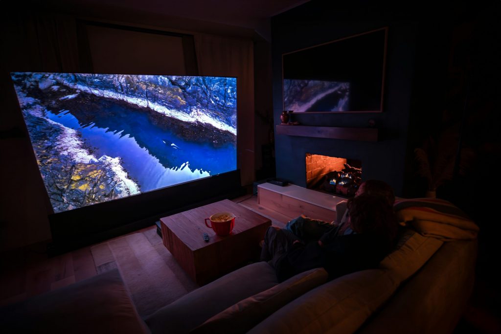 A cosy home theatre setup with a large screen, soft seating, fireplace, and dim ambient lighting for an immersive movie night experience.