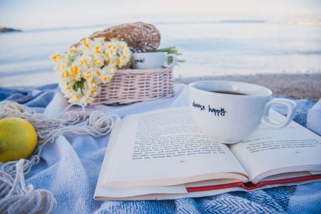 Cup of coffee resting on an open book beside a picnic basket on a beach, creating a relaxed UK staycation scene.