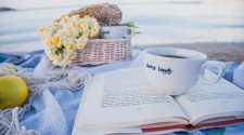 Cup of coffee resting on an open book beside a picnic basket on a beach, creating a relaxed UK staycation scene.