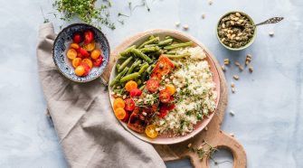 A balanced meal with grilled salmon, couscous, green beans, cherry tomatoes, pesto and pine nuts on a wooden board.