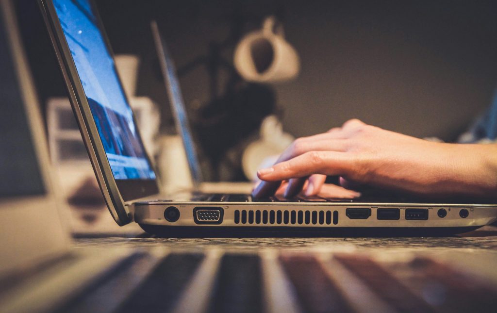 Close-up of a person typing on a laptop in a dimly lit setting, with a blurred coffee cup in the background.