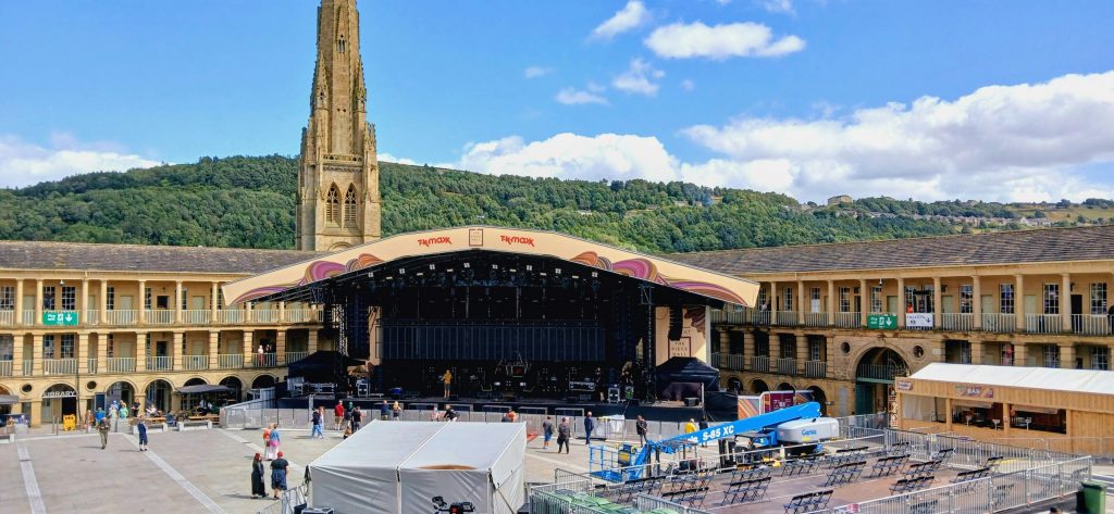 Outdoor stage set up in a historic Yorkshire courtyard with a church tower and green hillside in the background.