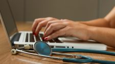 Healthcare professional working on a laptop beside a stethoscope, representing digital patient consultations and modern clinical care.