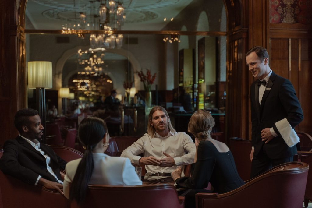 Business guests seated in a luxury private dining room while a waiter discusses the evening’s service, creating an executive dinner setting.