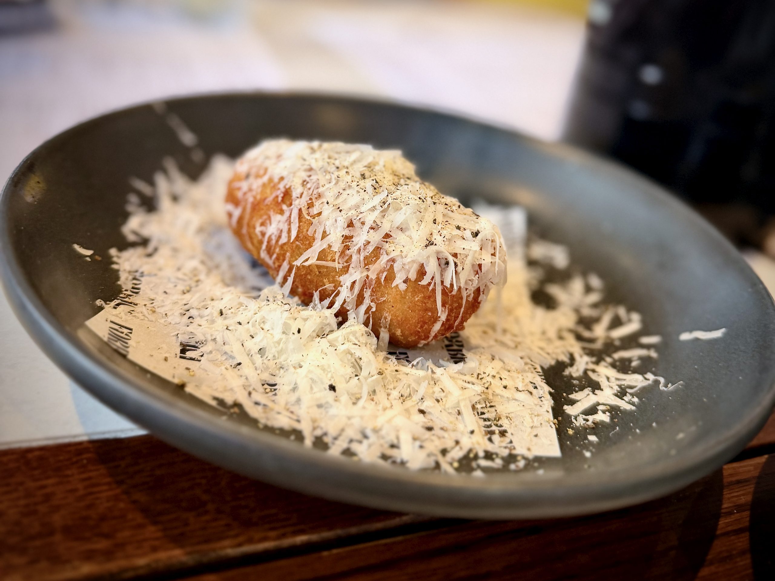 Golden cheese-covered croquettes in a black serving bowl