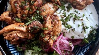 Chicken shawarma rice bowl served with fluffy rice, garlic yoghurt, pickled red onion, cucumber and chopped herbs in a patterned bowl.