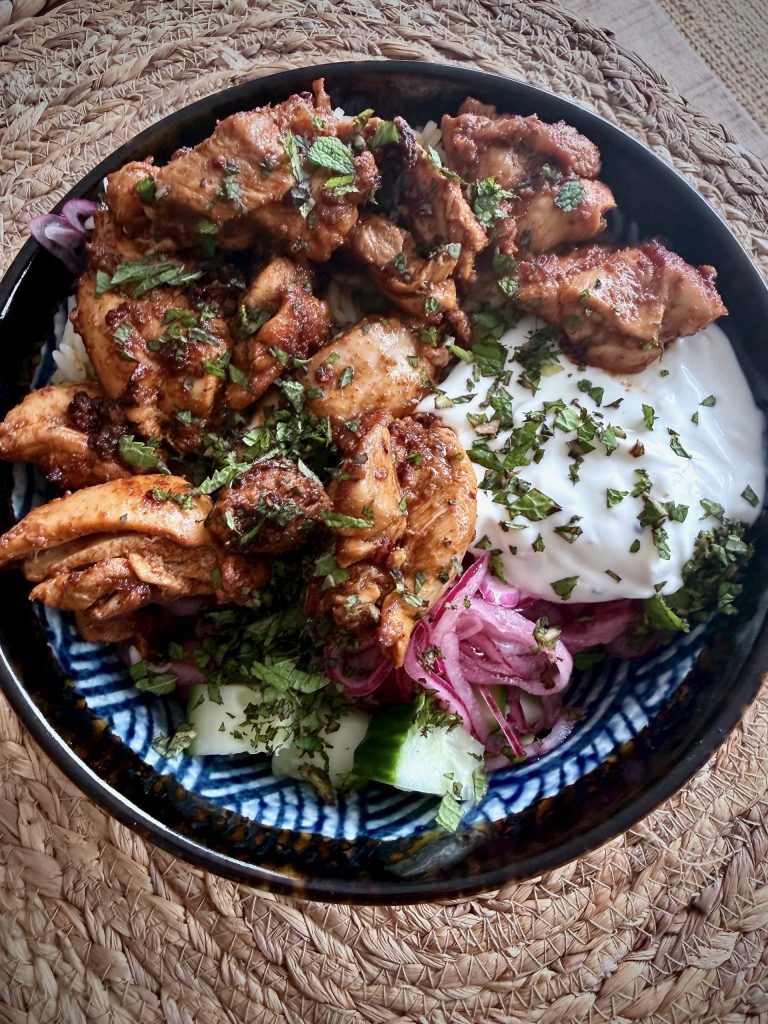 Chicken shawarma rice bowl served with fluffy rice, garlic yoghurt, pickled red onion, cucumber and chopped herbs in a patterned bowl.