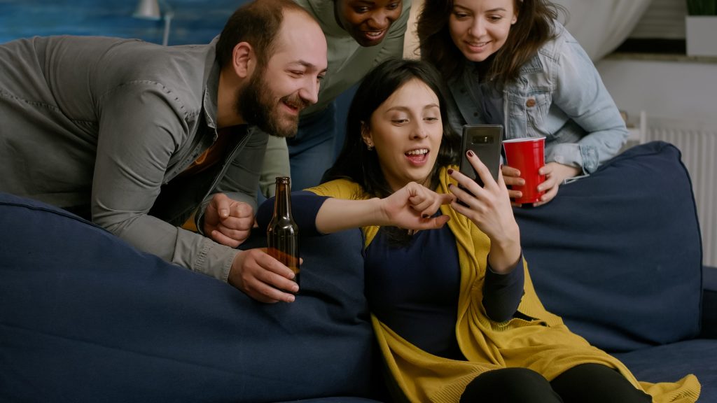 Group of young friends sitting on a sofa watching football or entertainment on a mobile phone together.