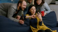 Group of young friends sitting on a sofa watching football or entertainment on a mobile phone together.