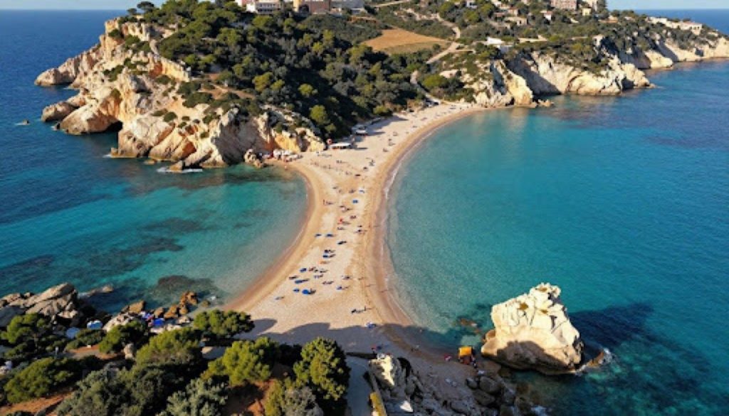 Aerial view of a curved sandy beach in Sicily with turquoise waters, rocky cliffs, and sunbathers along the shoreline.