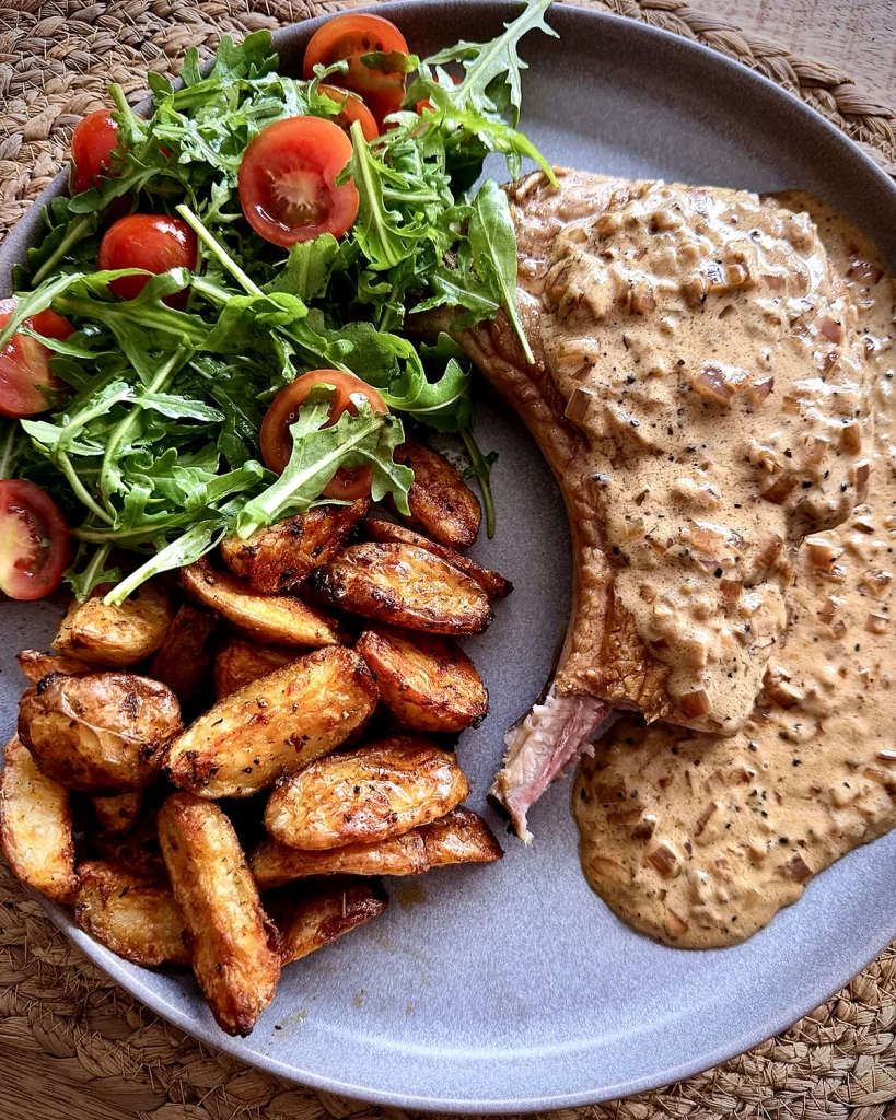 Steakhouse-style peppercorn pork chop with crispy garlic potatoes and rocket salad