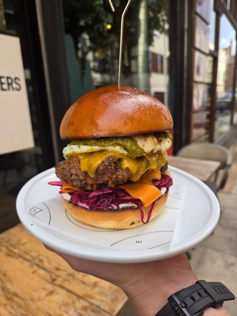 Burger layered with melted cheese, fried egg, green sauce and red cabbage at House of Koko Leeds