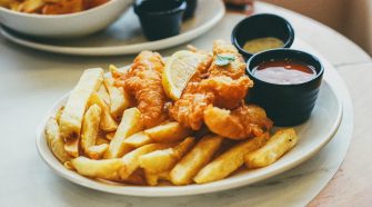 A plate of english fish and chips with ketchup and tarta sauce