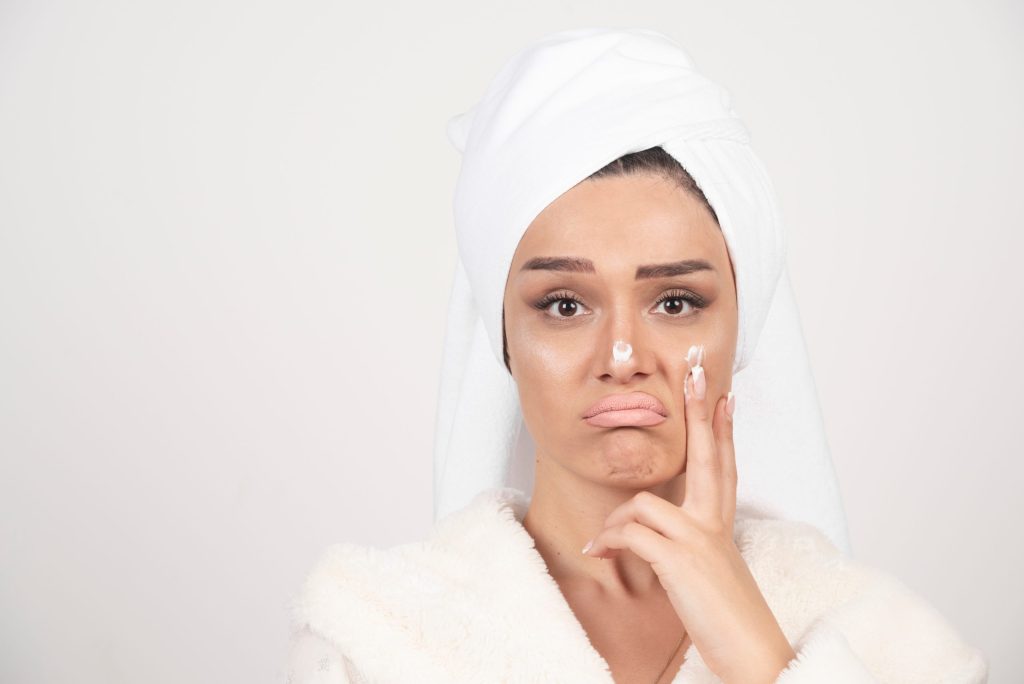 Woman with a towel wrapped around her hair applying face cream to her cheek
