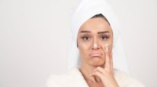 Woman with a towel wrapped around her hair applying face cream to her cheek