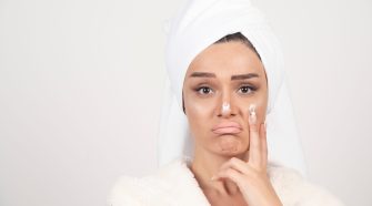 Woman with a towel wrapped around her hair applying face cream to her cheek