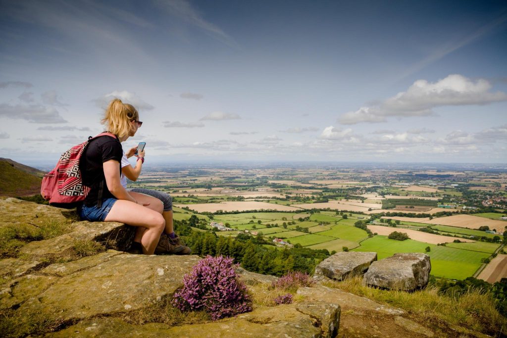 Walkers checking a smartphone on a rocky hillside overlooking Yorkshire countryside