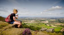 Walkers checking a smartphone on a rocky hillside overlooking Yorkshire countryside