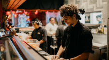 Chef preparing sushi at a counter with colleagues in a commercial kitchen